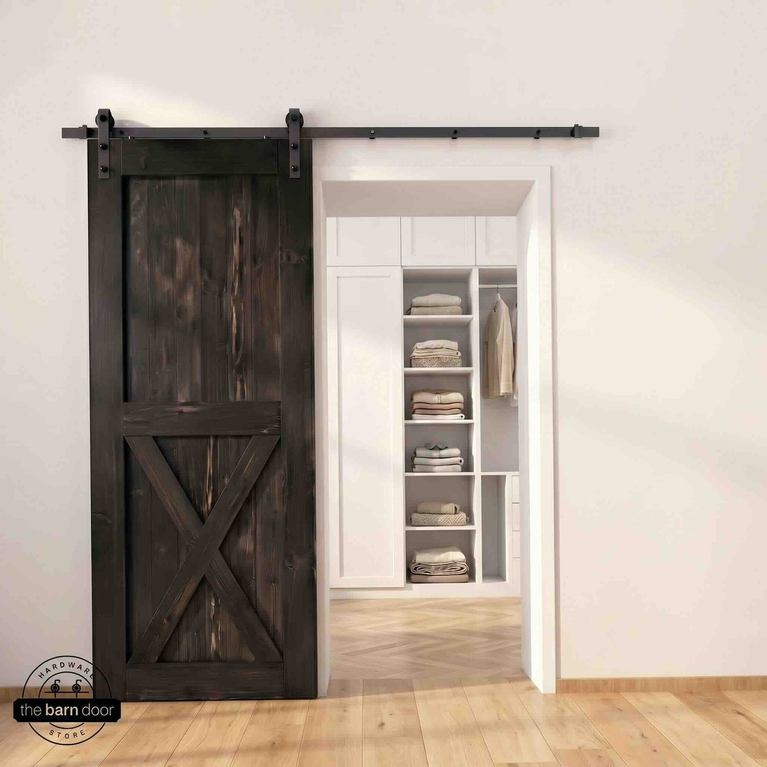Half-X barn door in ebony stain finish with matte black sliding barn door hardware, open to a white built-in closet with herringbone hardwood floors