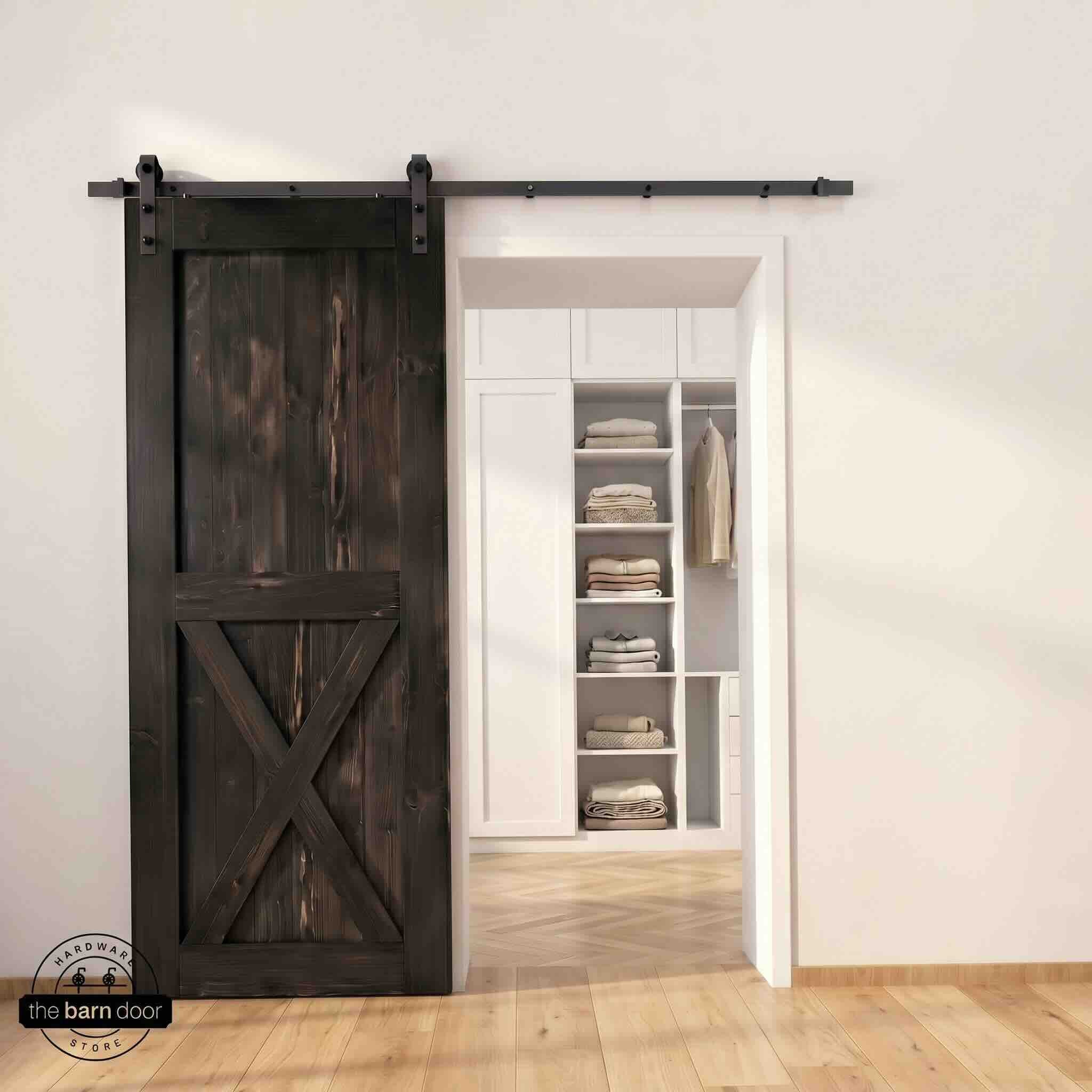 Half-X barn door in ebony stain finish with matte black sliding barn door hardware, open to a white built-in closet with herringbone hardwood floors
