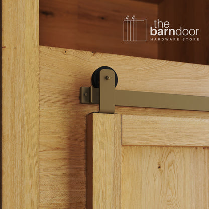 A close-up photograph of a sliding mini barn door on a natural oak cabinet, featuring gold top-mount straight hardware.