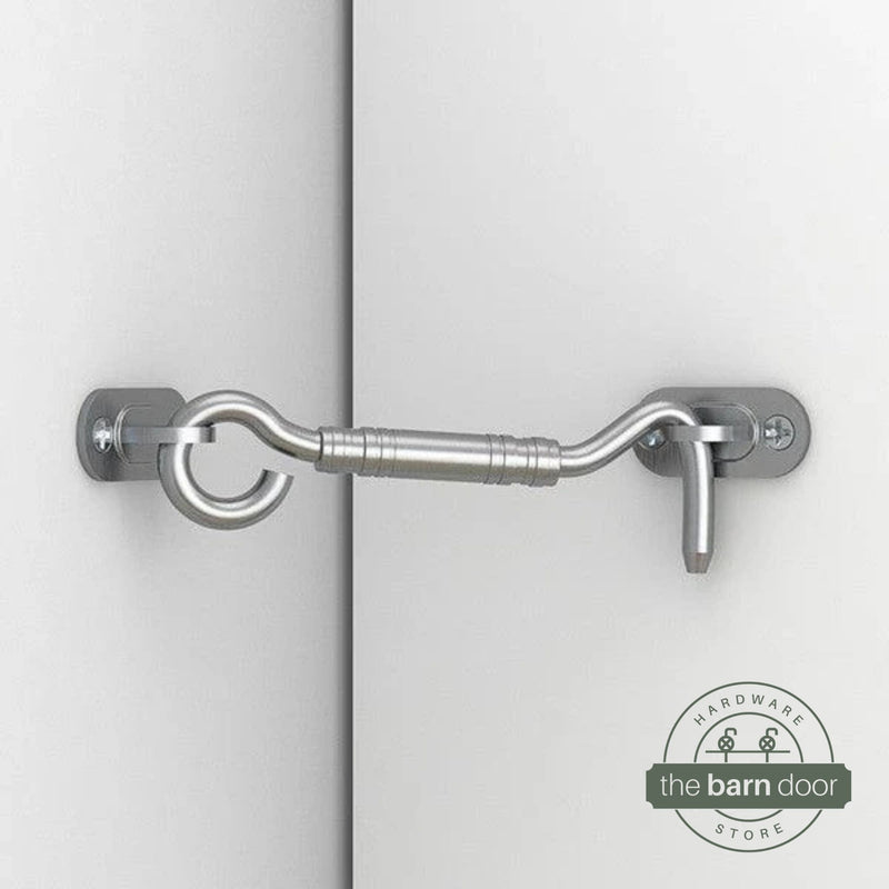 Stainless steel hook and eye barn door latch mounted on a white door securing it to the adjacent wall