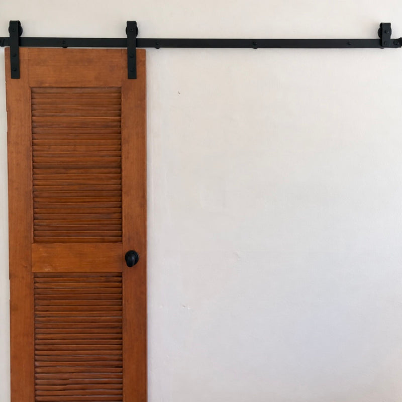 Wooden shutter door with black hardware on a white wall