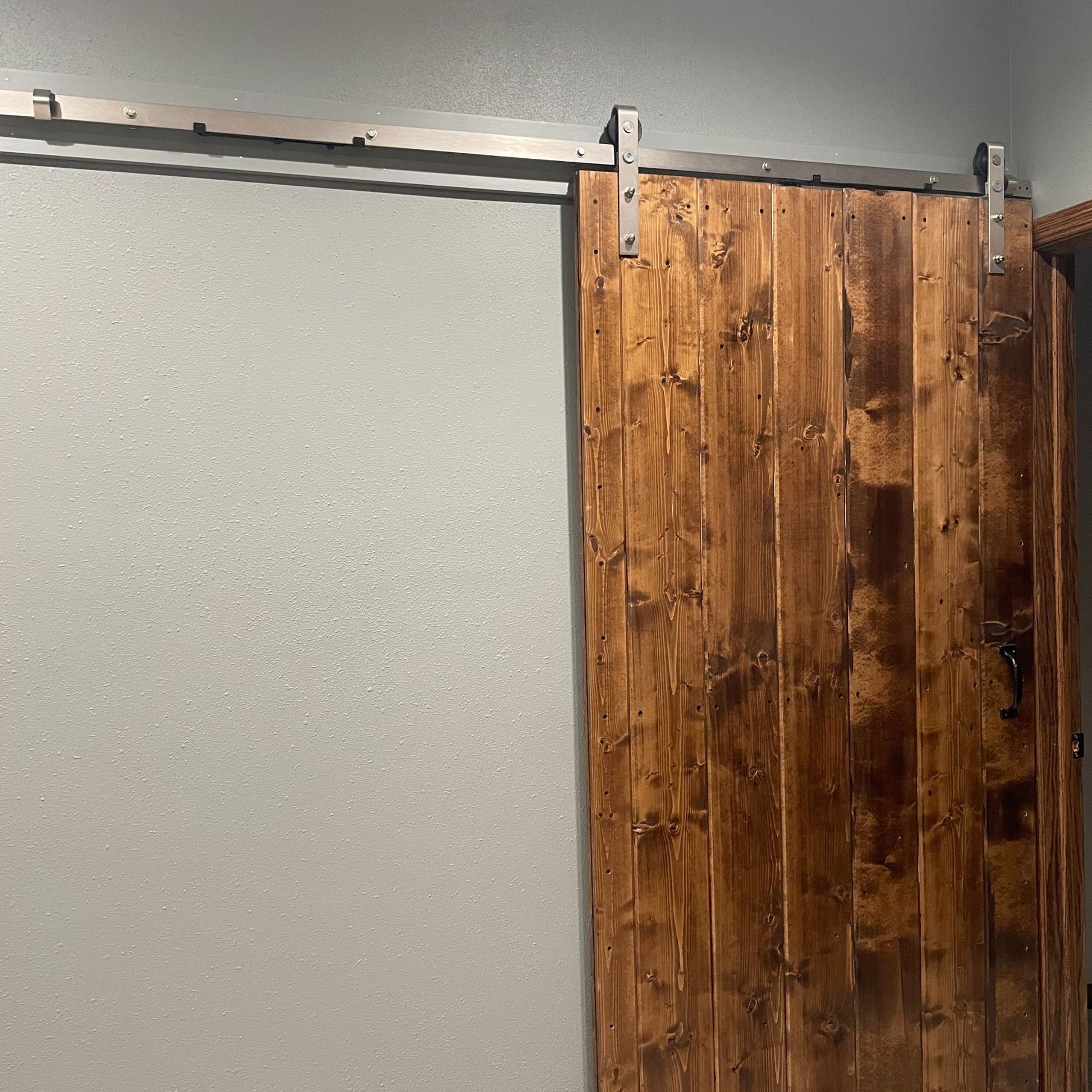 Wooden sliding barn door with j-strap brushed nickel barn door hardware on a gray wall