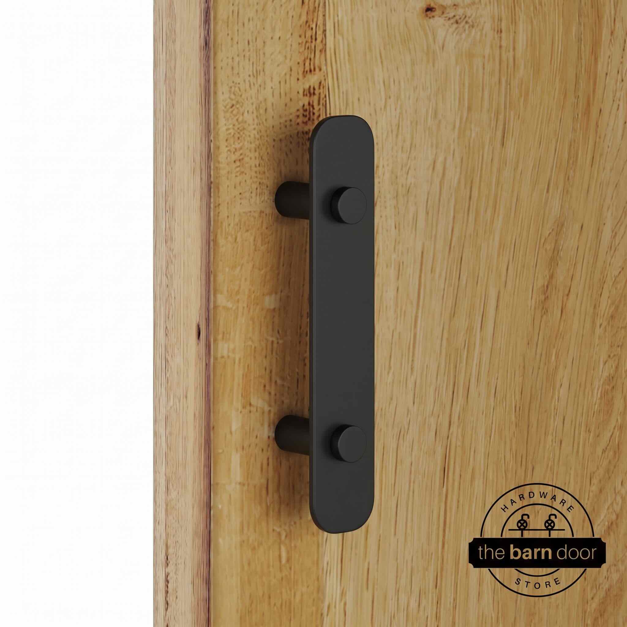 Matte black powder-coated stainless steel barn door flat bar pull handle on standoffs, mounted on a natural wood sliding barn door