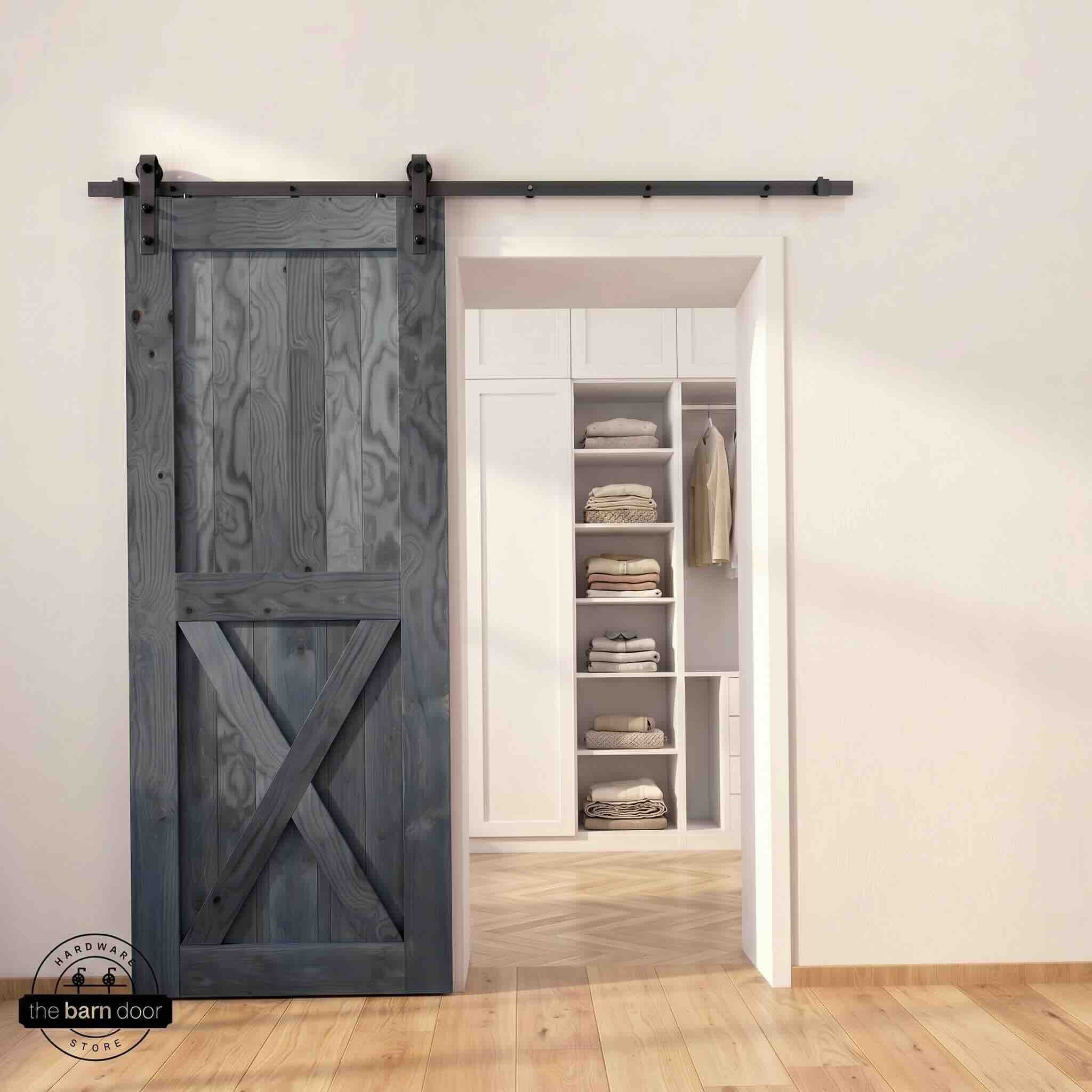 Half-X barn door in navy stain finish with matte black sliding barn door hardware, open to a white built-in closet with herringbone hardwood floors