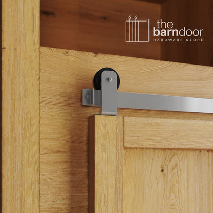 A close-up photograph of a sliding mini barn door on a natural oak cabinet, featuring PC Chrome top-mount straight hardware.
