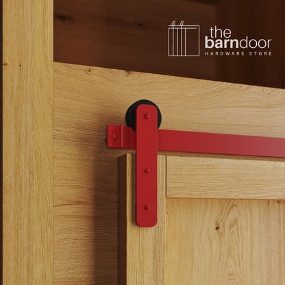 A close-up photograph of a natural oak cabinet with a sliding mini barn door, featuring a red straight-strap hanger and a red track system.