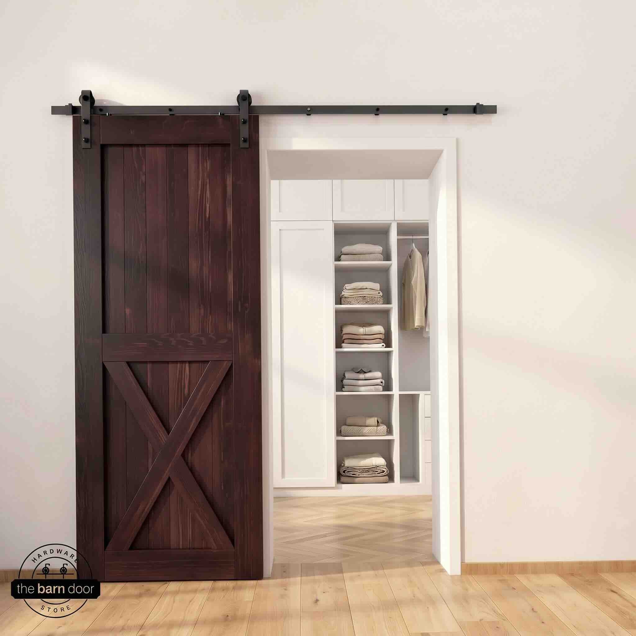 Half-X barn door in red mahogany stain finish with matte black sliding barn door hardware, open to a white built-in closet with herringbone hardwood floors