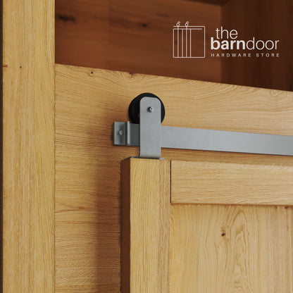 A close-up photograph of a sliding mini barn door on a natural oak cabinet, featuring silver metallic top-mount straight hardware.