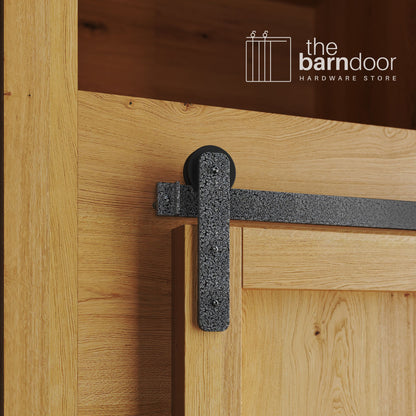 A close-up photograph of a natural oak cabinet with a sliding mini barn door, featuring a silver vein straight-strap hanger and a silver vein track system.