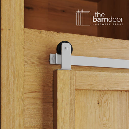 A close-up photograph of a sliding mini barn door on a natural oak cabinet, featuring white top-mount straight hardware.