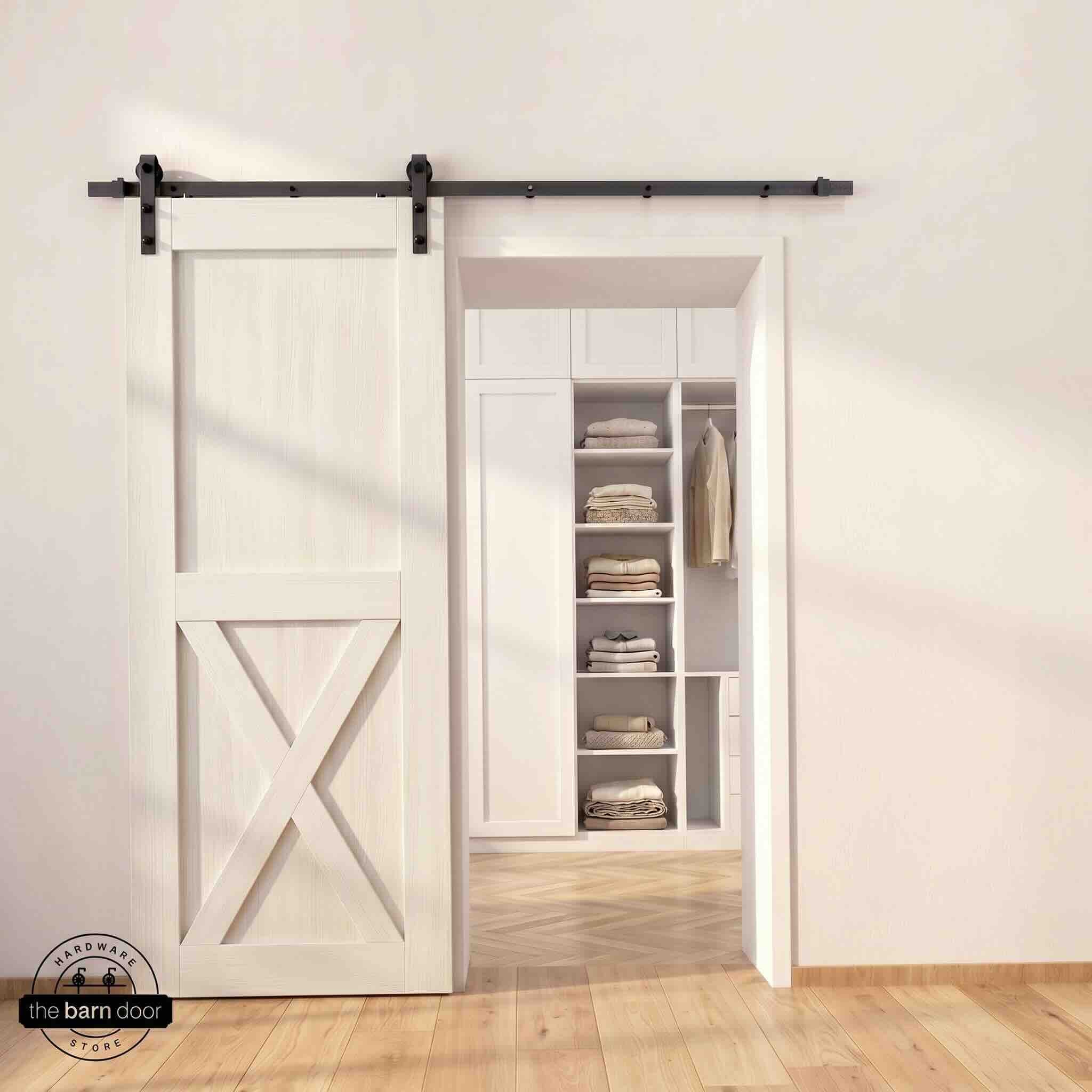 Half-X barn door in white stain finish with matte black sliding barn door hardware, open to a white built-in closet with herringbone hardwood floors
